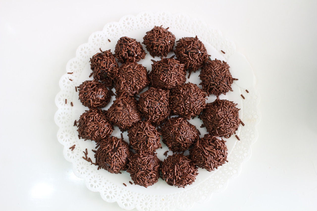 Brigadeiros enrolados e cobertos com granulado, servidos em forminhas sobre um prato