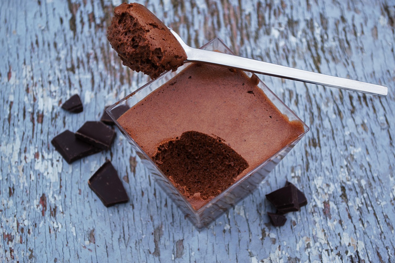 Brigadeiro cremoso servido em potinho individual, com uma colherada erguida e pedaços de chocolate ao lado