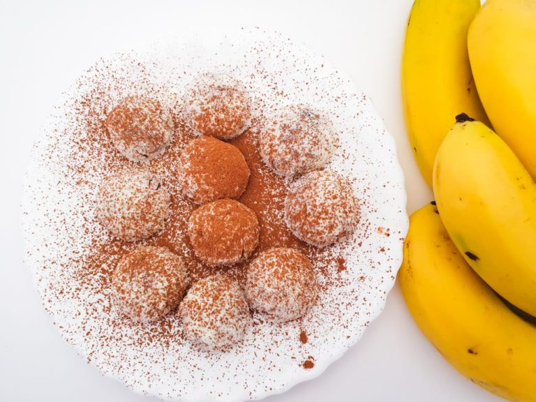 Brigadeiros de banana com cacau vistos de cima ao lado de bananas frescas