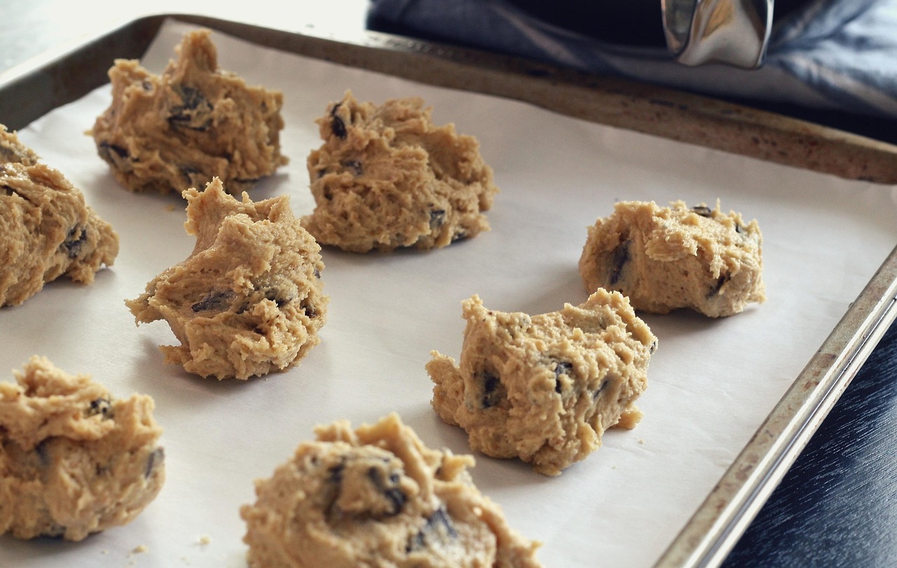 Bolinhas de massa de cookie com gotas de chocolate dispostas numa assadeira forrada, prontas para assar
