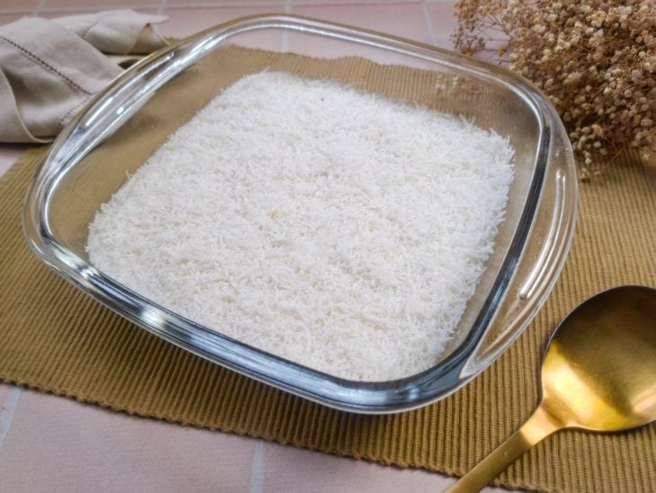 Refratário de vidro com cuscuz de tapioca coberto de coco ralado sobre um jogo americano