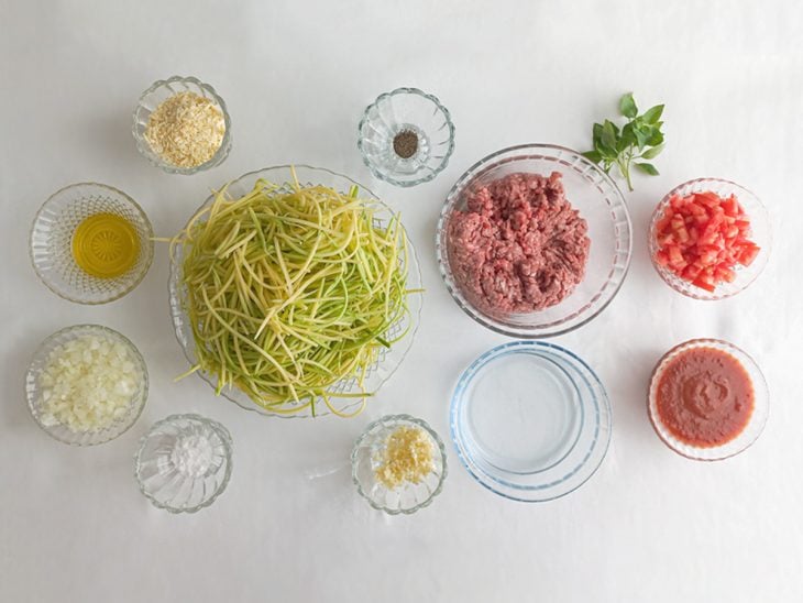 Ingredientes do espaguete de abobrinha à bolonhesa organizados na bancada: abobrinha em fios, carne moída, tomate, alho e molho de tomate