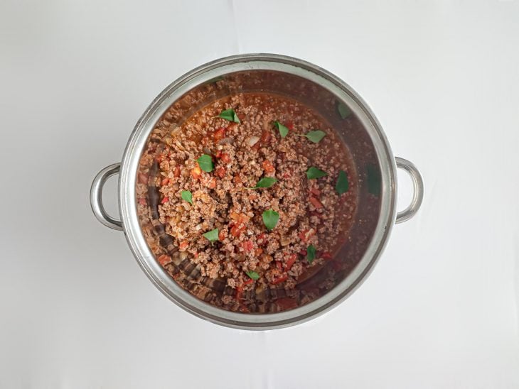 Molho bolonhesa pronto numa panela, com carne moída, tomate e folhas de manjericão