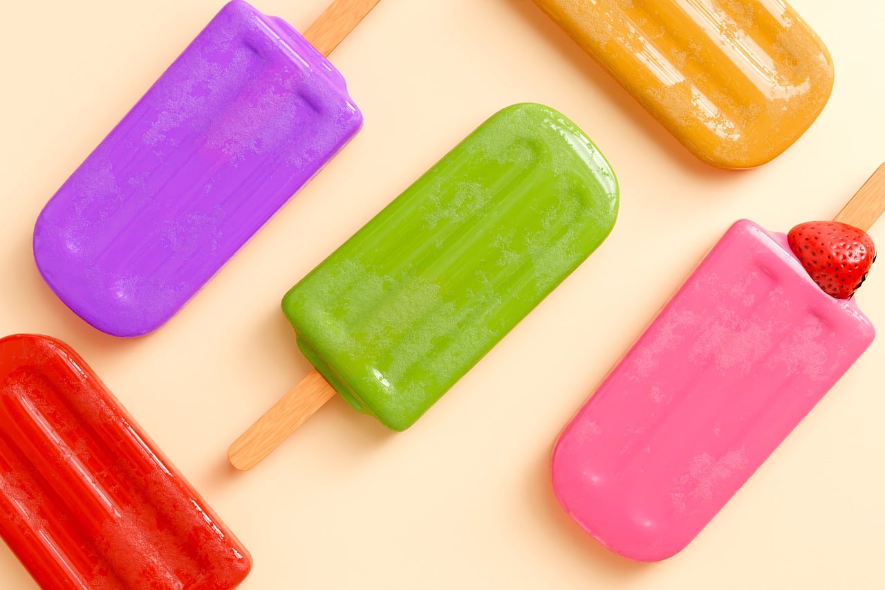 Picolés coloridos de sabores variados vistos de cima sobre fundo claro