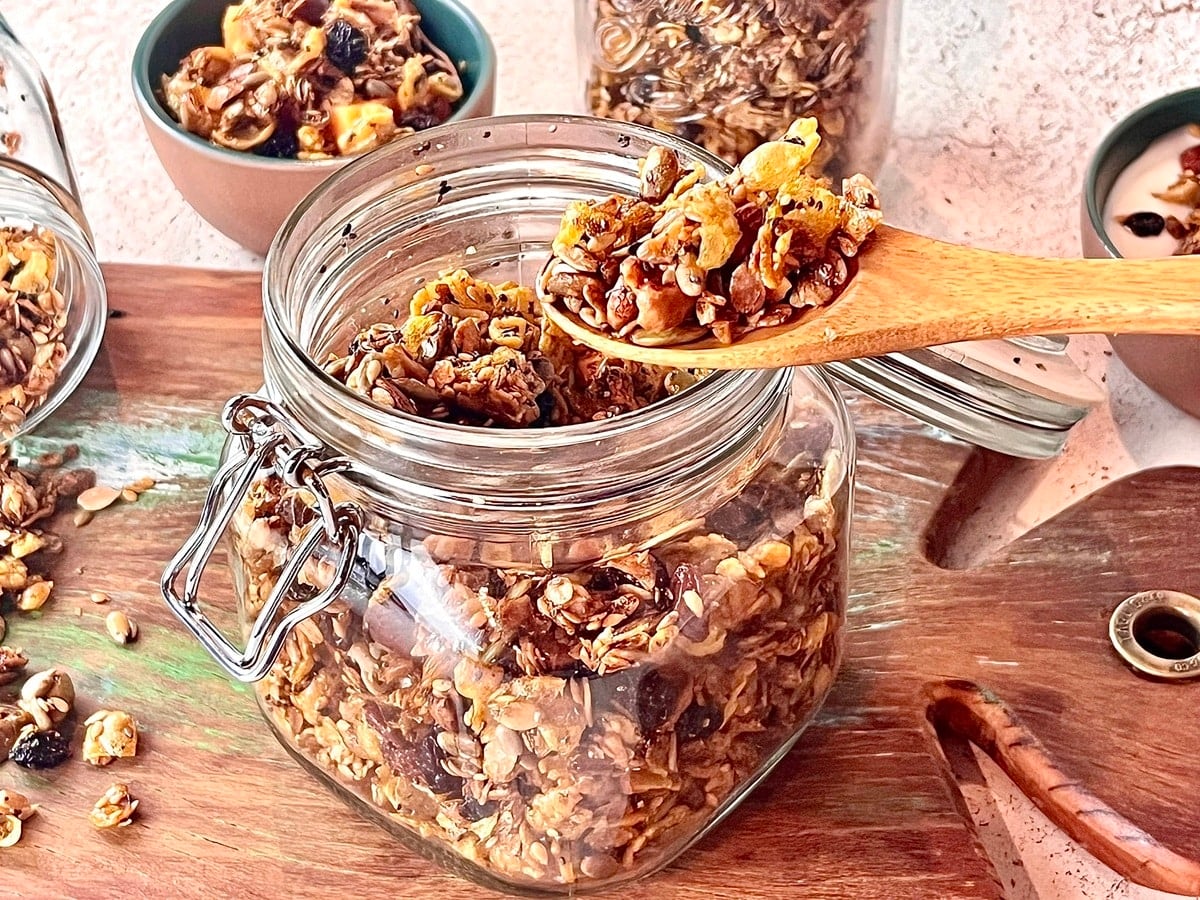 Granola crocante sendo servida com colher de pau dentro de um pote de vidro