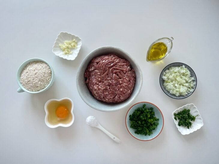 Ingredientes do hambúrguer fit organizados sobre a bancada: carne moída, aveia, ovo, alho, cebola e cebolinha