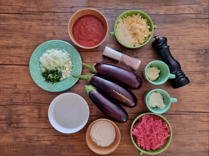 Ingredientes crus da lasanha de berinjela: berinjelas inteiras, carne moída, molho de tomate, cebola, alho e queijos sobre a bancada