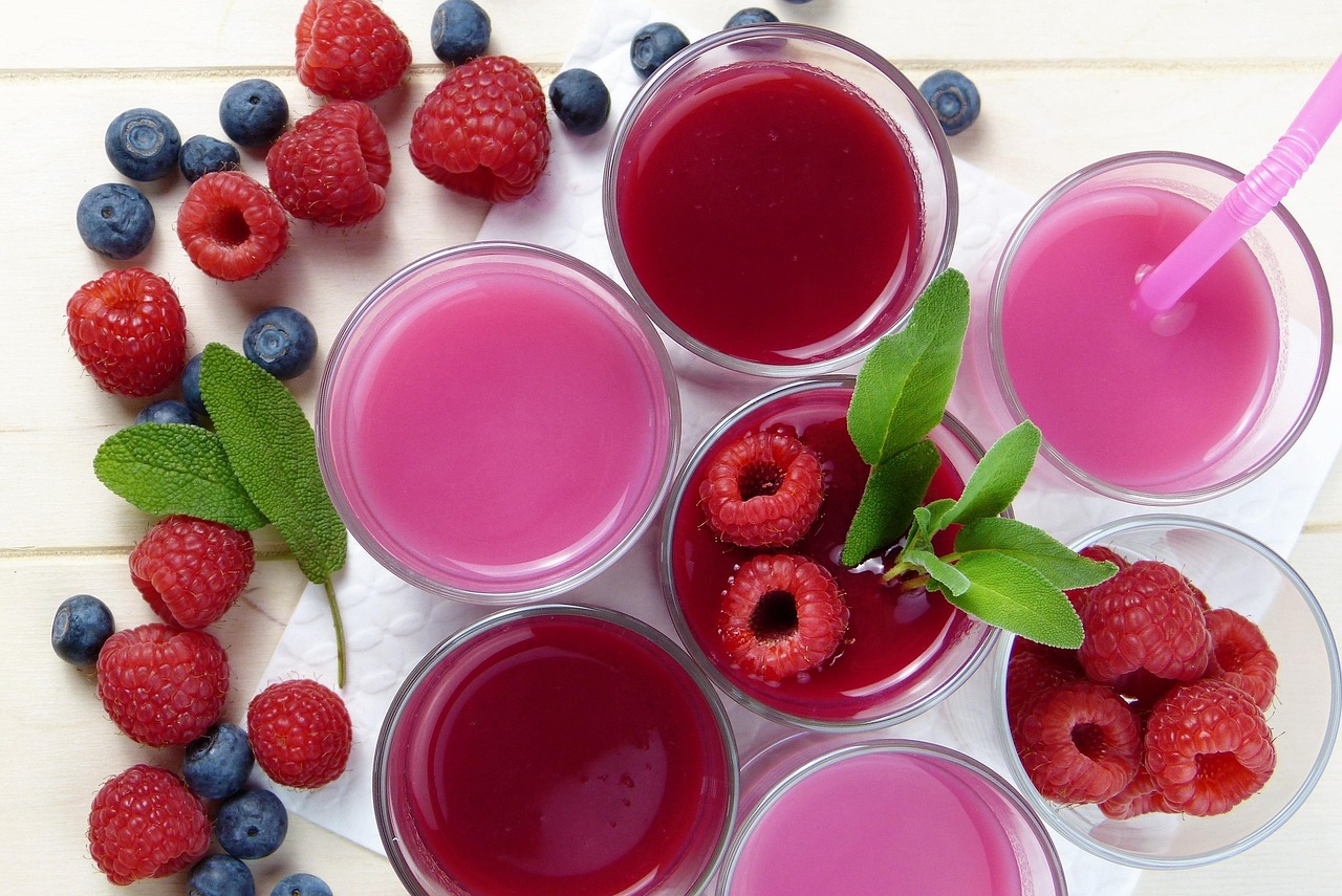 Framboesas e mirtilos frescos ao lado de taças com suco de frutas vermelhas