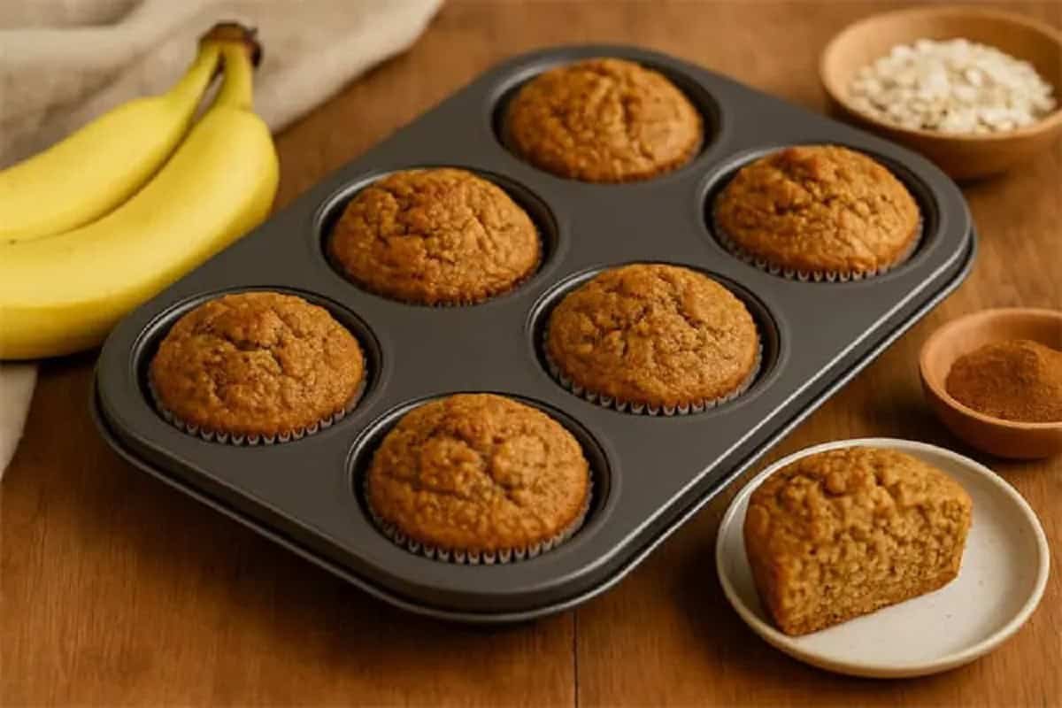 Muffins de banana e aveia dourados na forma, ao lado de bananas e canela