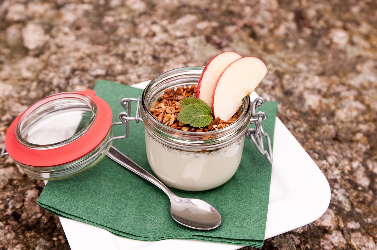 Overnight oats servido em potinho de vidro com granola, fatias de maçã e uma colher ao lado