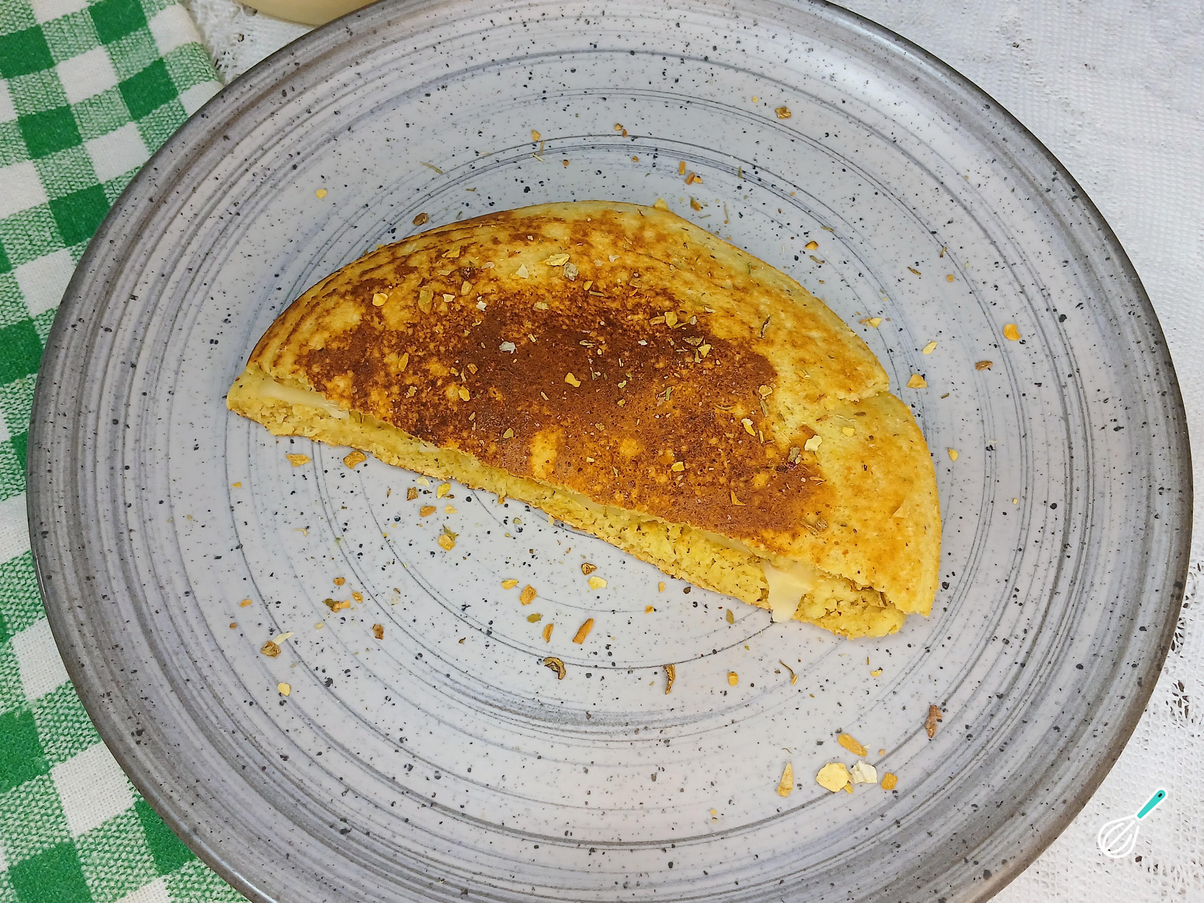 Pão de frigideira dobrado ao meio com queijo derretido por dentro, num prato