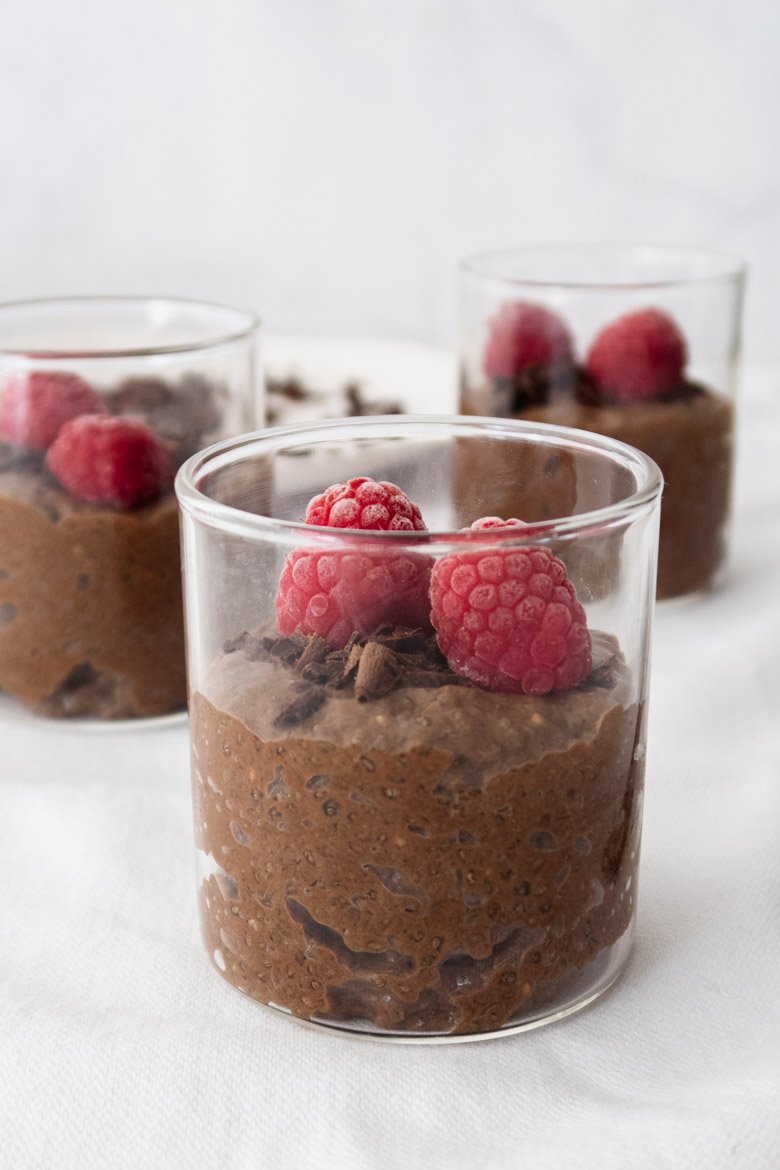 Pudim de chia achocolatado em copo de vidro, com framboesas e raspas de chocolate