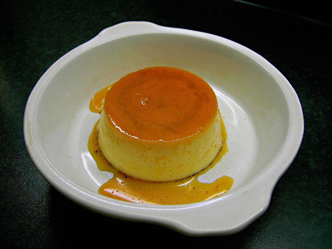 Pudim de leite desenformado em prato individual, coberto de calda de caramelo