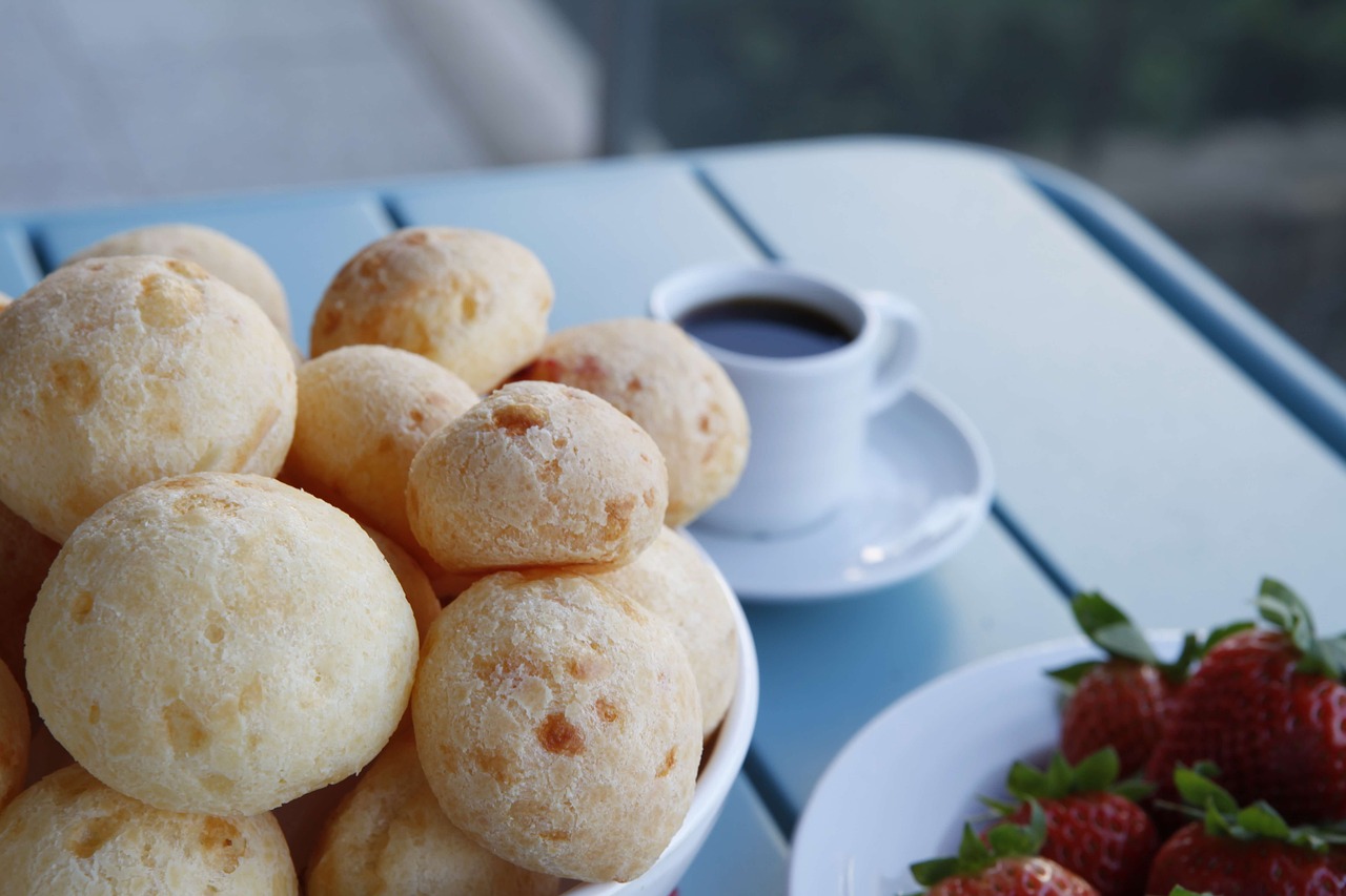 Pão de queijo empilhado em uma tigela ao lado de uma xícara de café