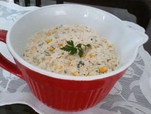 Salpicão cremoso com milho servido numa tigela vermelha, decorado com salsinha