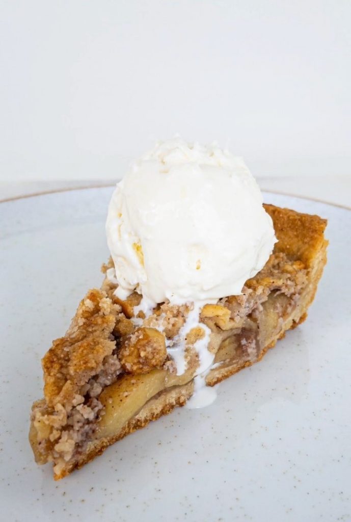 Fatia de torta de maçã com massa e cobertura crumble servida com uma bola de sorvete de creme (versão com massa amanteigada)